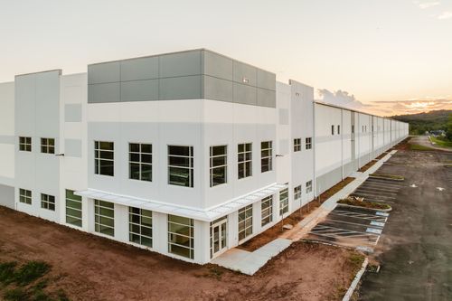 Aerial view of a large white and gray two-story commercial building with tinted windows at dusk
