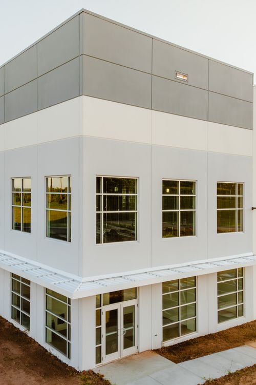Corner of a commercial building with gray upper panels, cream cladding and rows of windows