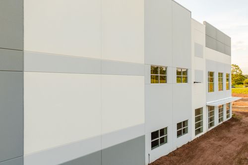 Angled corner of a white commercial building with gray trim and glowing windows at dusk