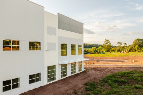 Aerial view of a long warehouse with loading dock doors beside a graded construction lot