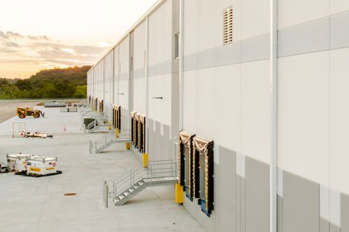 Angled warehouse wall with a gray accent band, vents and metal panel siding at sunset