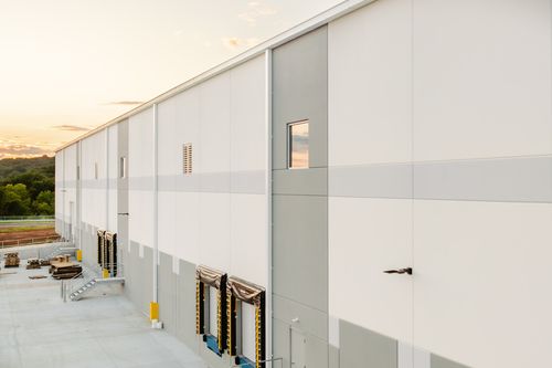 Small corner window reflecting the sunset sky on a white and gray building panel