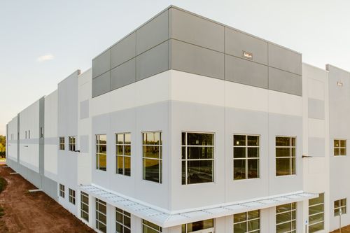 Angled view of a two-tone commercial facade with a gray accent panel and glowing windows at sunset
