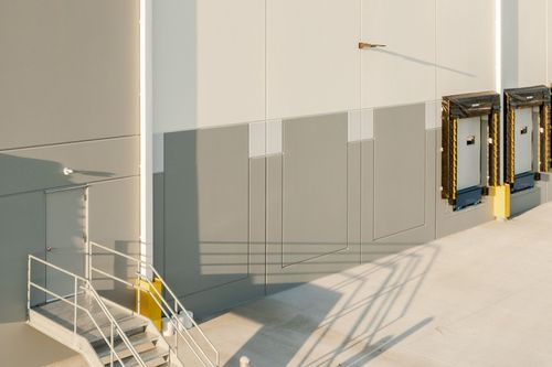 Angled warehouse wall with vents, a small window and dock doors with yellow bumpers