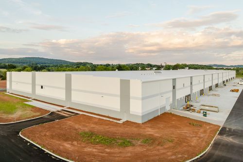 Angled view of a cream metal panel warehouse wall with a gray accent stripe and walkway