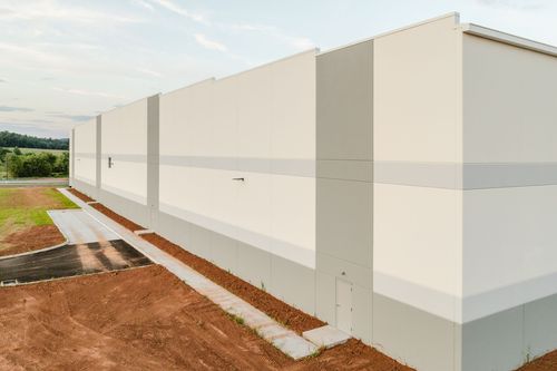 Angled corner of a white commercial building with a gray accent stripe and small access door