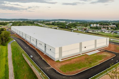 Angled warehouse wall with a small window and gray accent stripe over a graded lot