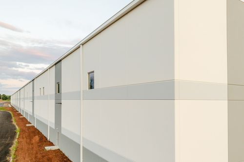 Small square window and gray access door centered on a cream metal panel wall