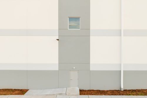 Vertical stripe of a small window and light fixture on cream and gray metal siding