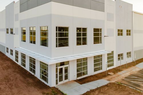 Corner of a white commercial building with gray trim panels and a glass entry door
