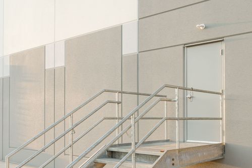 Metal stairway and railing leading to a gray access door on a commercial building