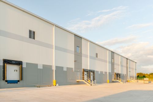 Angled view of a warehouse wall with loading dock doors and stairways at sunset