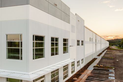 Aerial view of a long white commercial building with a gray accent stripe at sunset