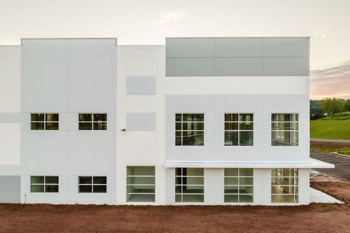 Long warehouse wall with a vent and gray accent stripe under a soft sunset sky