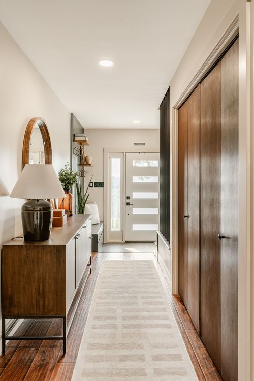 Entryway with a wood console table, arched mirror, table lamp and runner rug leading to a glass front door