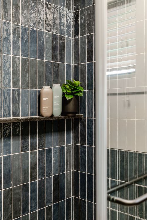 Glass shower door beside navy tile with a built-in shelf and window view