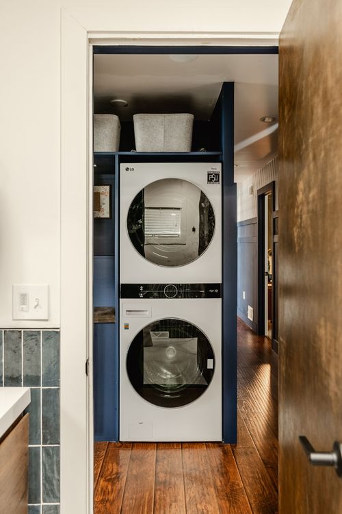 Stacked LG washer and dryer in a navy laundry nook off a wood hallway