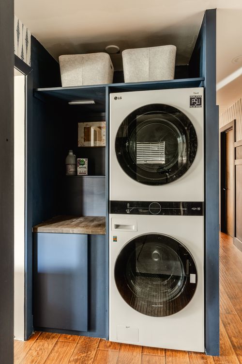 Laundry closet with navy paneling, stacked white washer-dryer and storage baskets