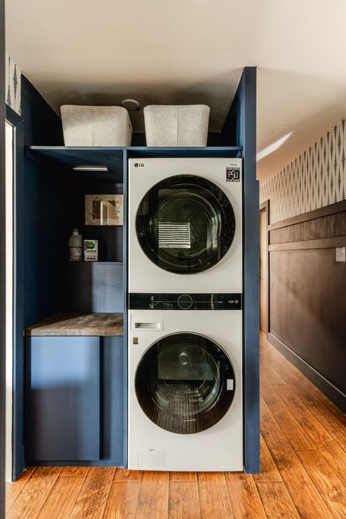 Stacked LG washer-dryer set in a navy laundry closet with a wood folding counter
