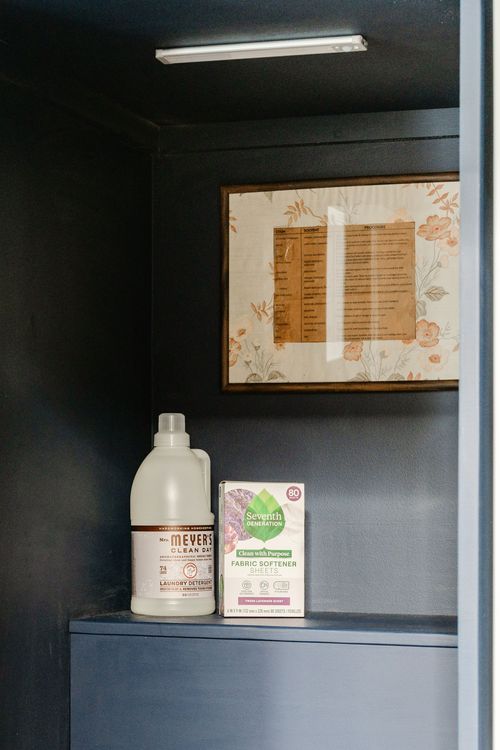 Framed vintage laundry instructions and detergent bottles on a dark laundry shelf