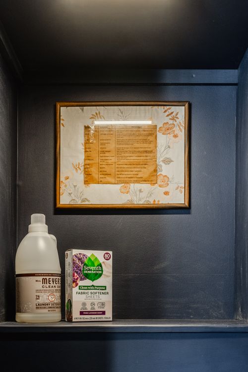 Close-up of a framed vintage laundry chart above detergent on a navy shelf
