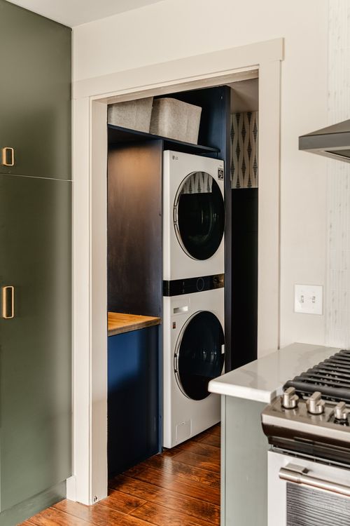 Hallway view into a navy laundry nook with stacked washer-dryer beside the kitchen