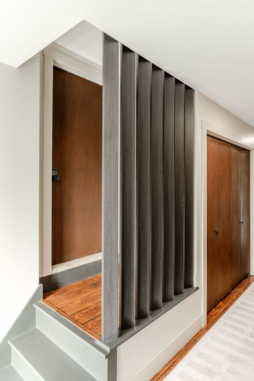 Wood slat room divider between a stairway landing and a hallway with paneled doors