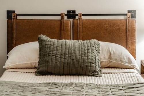 Close-up of a leather headboard with metal frame and olive throw pillow