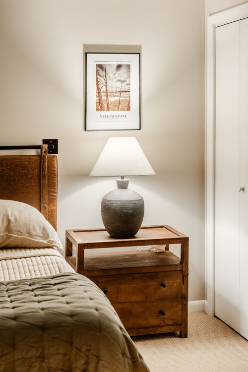 Nightstand with a stoneware lamp, framed print and wood dresser beside the bed