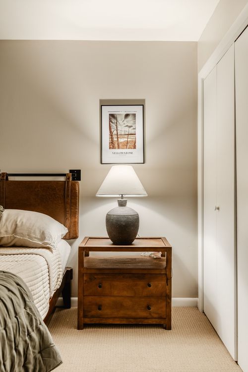 Wood nightstand with ceramic lamp and framed Yellowstone print beside a leather headboard