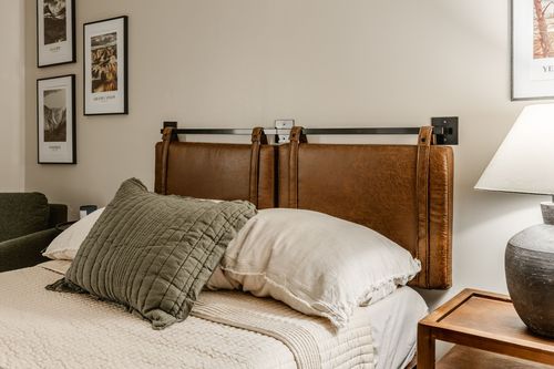 Leather headboard bed with layered pillows beneath a gallery of framed prints