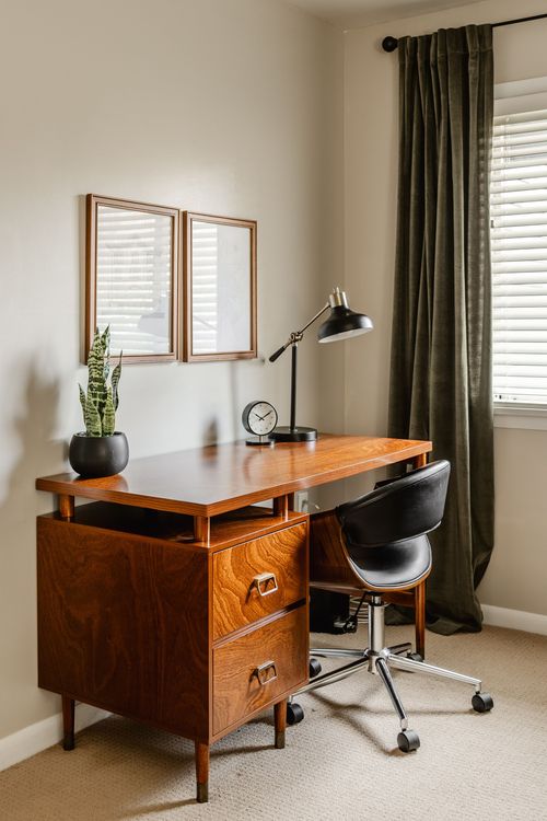 Mid-century wood desk with black task lamp, clock and rolling office chair
