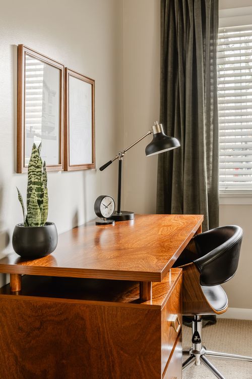 Close-up of a wood desk with brass lamp, small clock and black leather chair