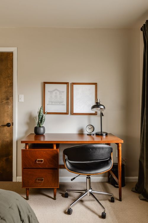Home office corner with vintage wood desk, framed prints and rolling chair