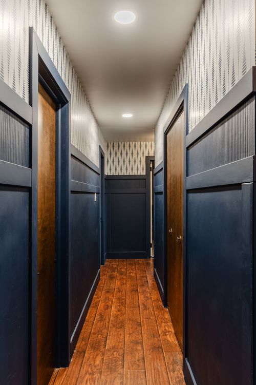 Hallway with navy wainscoting, patterned wallpaper and warm wood plank flooring