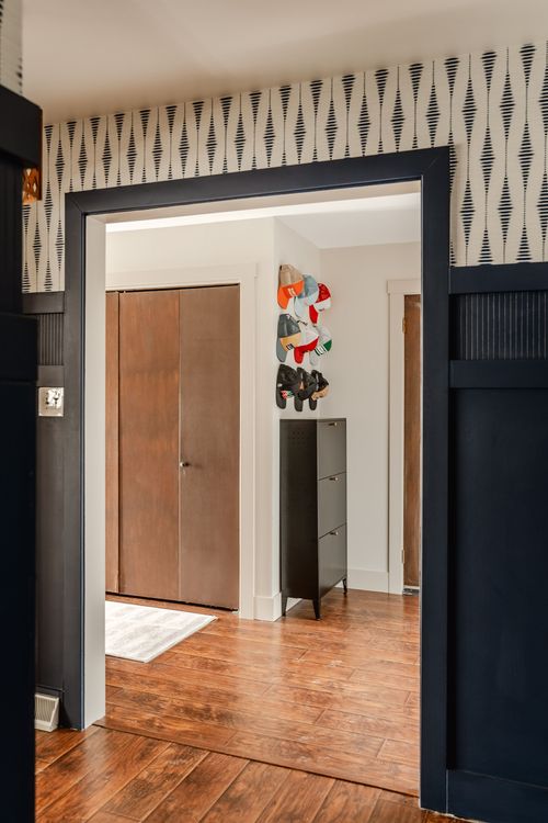 Entry view through navy trim into a mudroom with hooks of caps and a metal cabinet