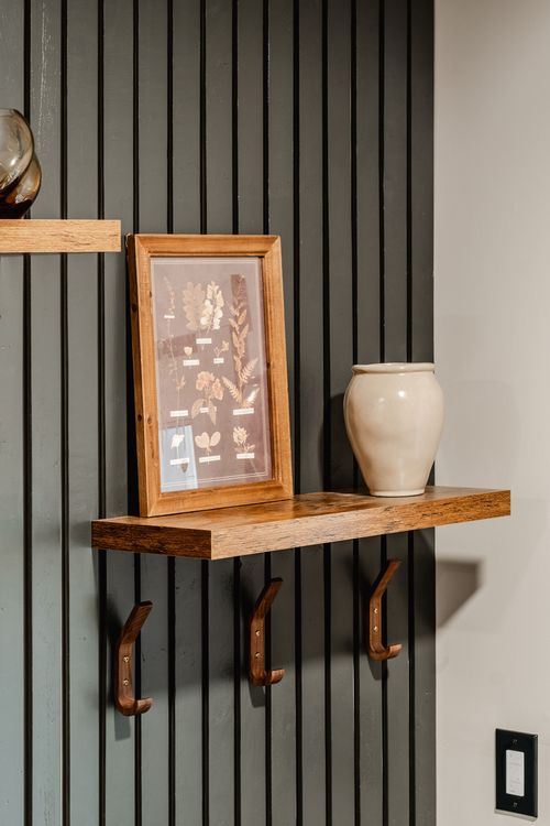 Wall shelf with a framed botanical print, leather coat hooks and a ceramic vase