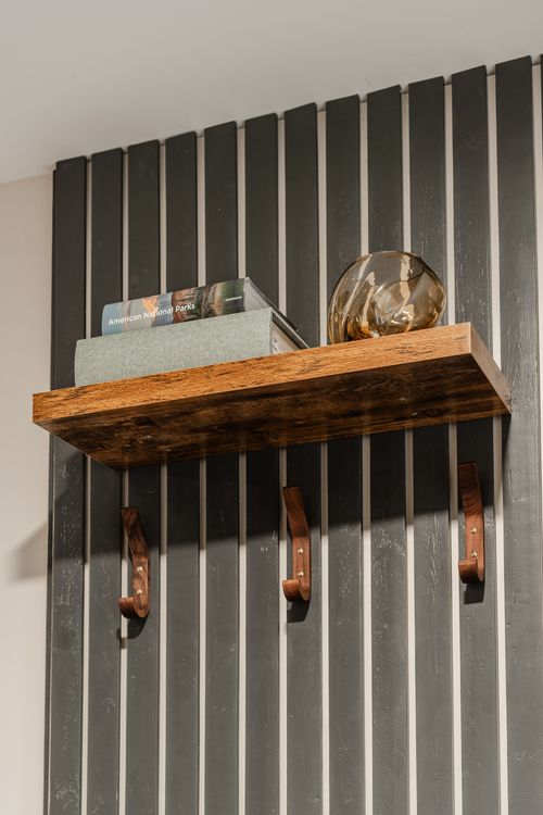 Wall shelf styled with books, an amber glass sphere and leather coat hooks