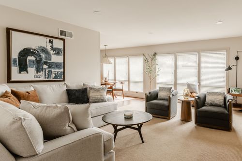 Living room with a beige sectional sofa, abstract art and armchairs by shuttered windows