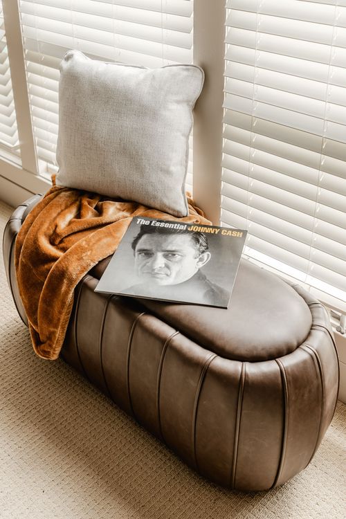 Leather channel-tufted ottoman with a pillow, throw blanket and record album