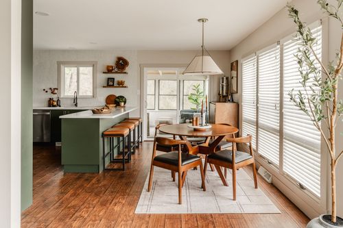 Dining nook with a round wood table, leather chairs and a pendant light off an open kitchen