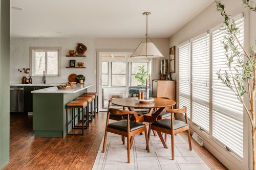 Kitchen with green cabinetry opening into a dining area with a round table and pendant light