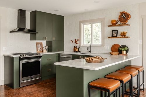 Kitchen with olive green cabinetry, black range hood and leather counter stools