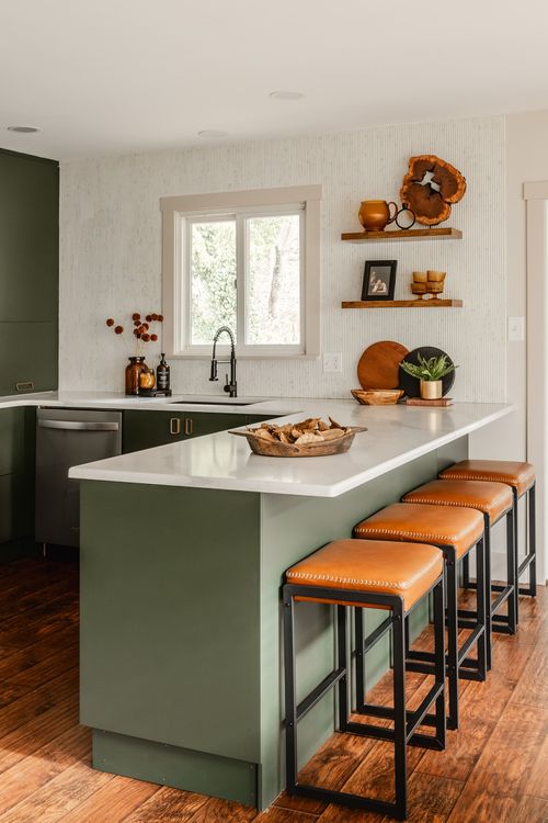 Kitchen sink area with green cabinets, a black faucet and floating shelves with glassware