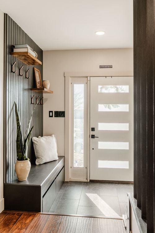 Entryway bench with a cushion beside a wood slat wall and white paneled front door