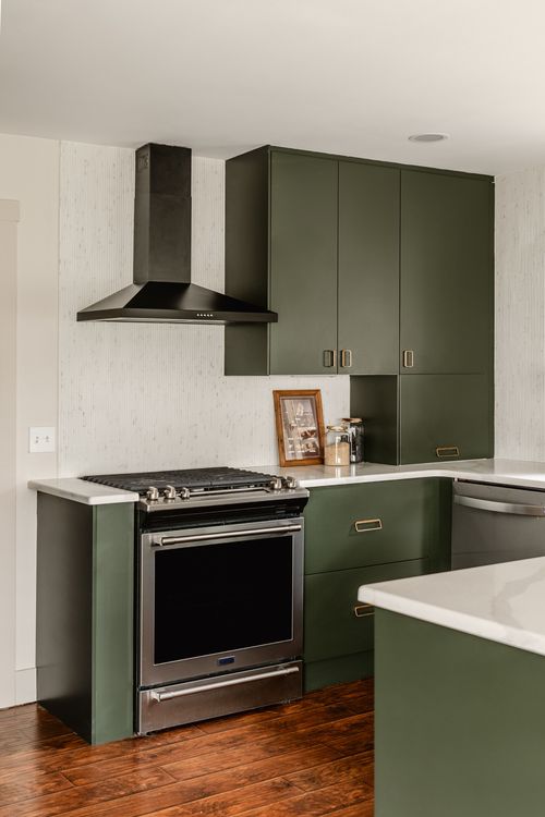 Kitchen range with a black hood over a gas cooktop flanked by green cabinetry