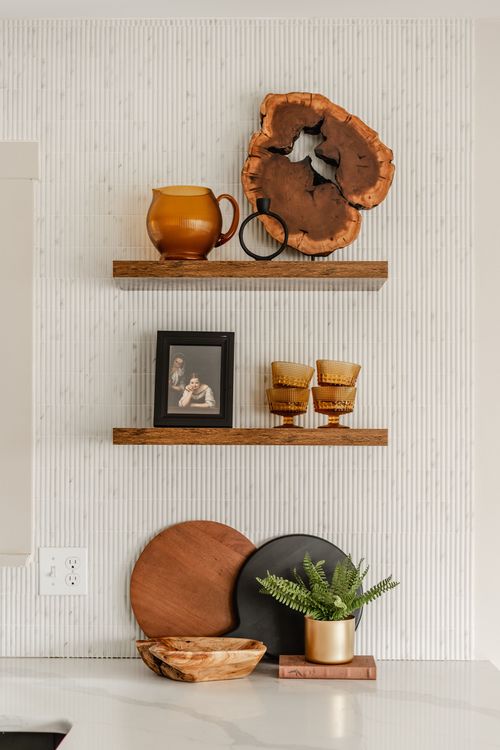 Close-up of styled open shelves with an amber pitcher, live-edge wood art and amber glasses