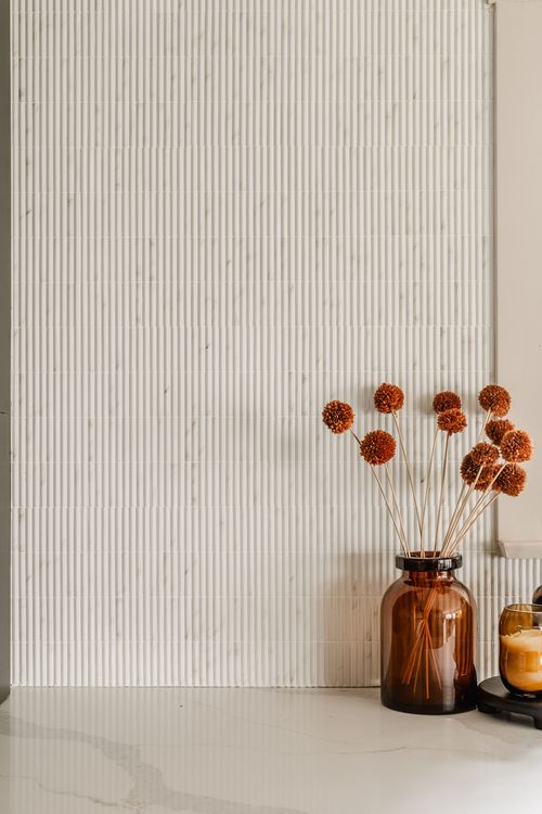 Close-up of dried flower stems in an amber glass vase against a tiled backsplash