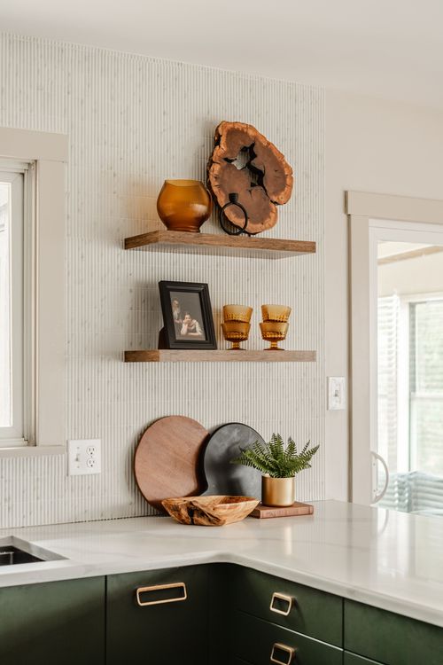 Floating shelves with amber pottery and a live-edge wood piece above a green cabinet corner