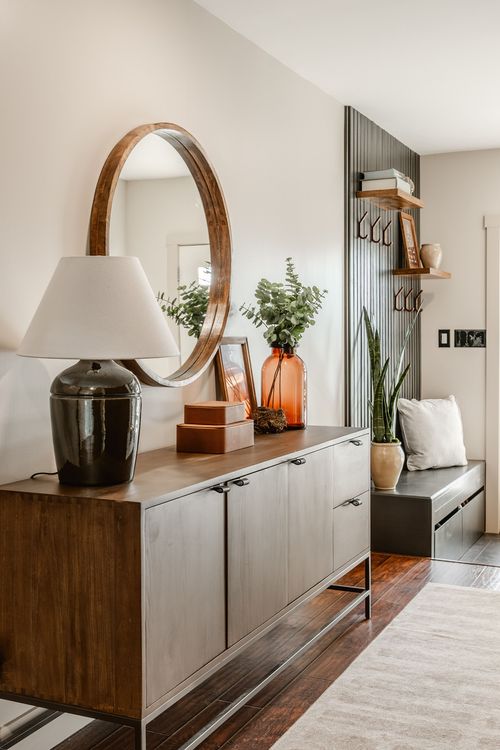 Round wood-framed mirror above a two-tone console table with a lamp and eucalyptus vase